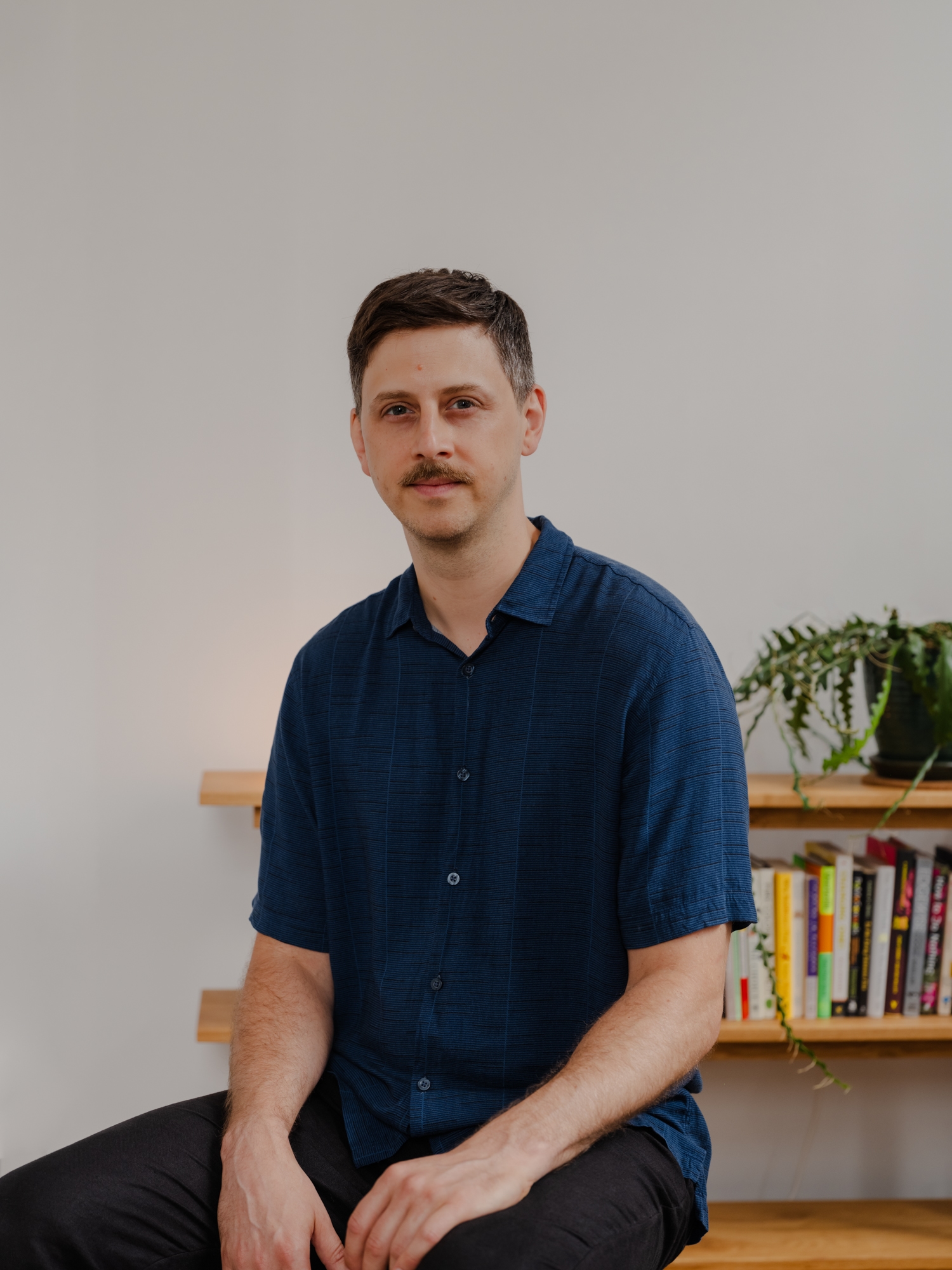 Carl in a blue shirt in front of a bookshelf with a plant and books.